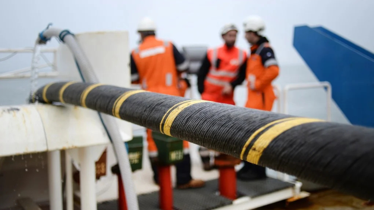 Closeup of undersea cable on ship with crew in safety gear in background