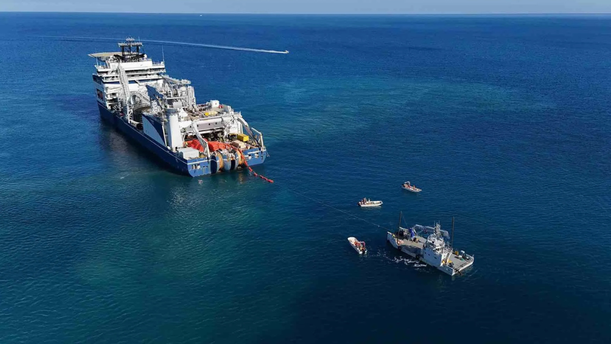 Large subsea cable-laying vessel deploying power cables with support boats