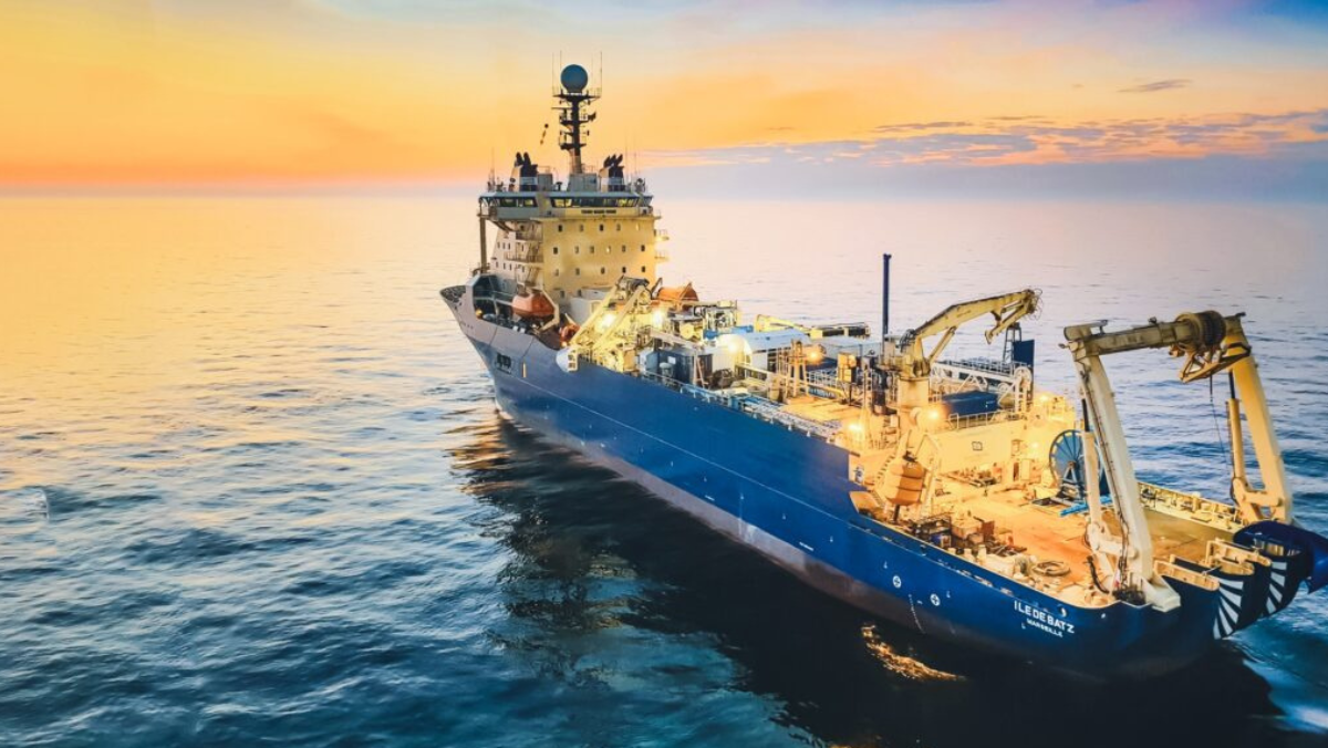 Offshore subsea cable vessel sailing during sunset with deck equipment illuminated